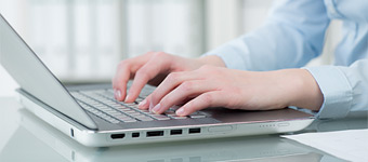 Ausschnitt einer an einem Laptop arbeitenden Frau, der tippende Hände zeigt.